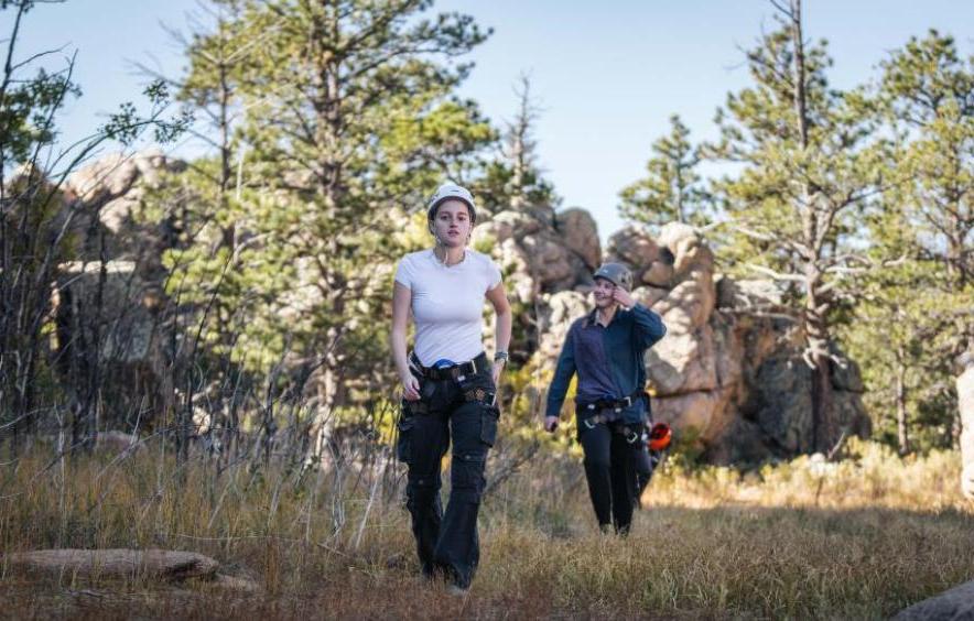 two students walking through clearing wearing climbing gear